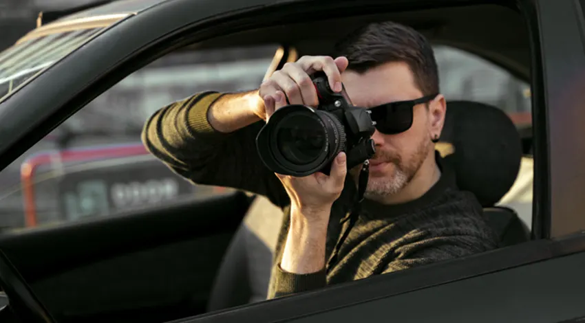 Détective privé photographiant au téléobjectif depuis un véhicule banalisé