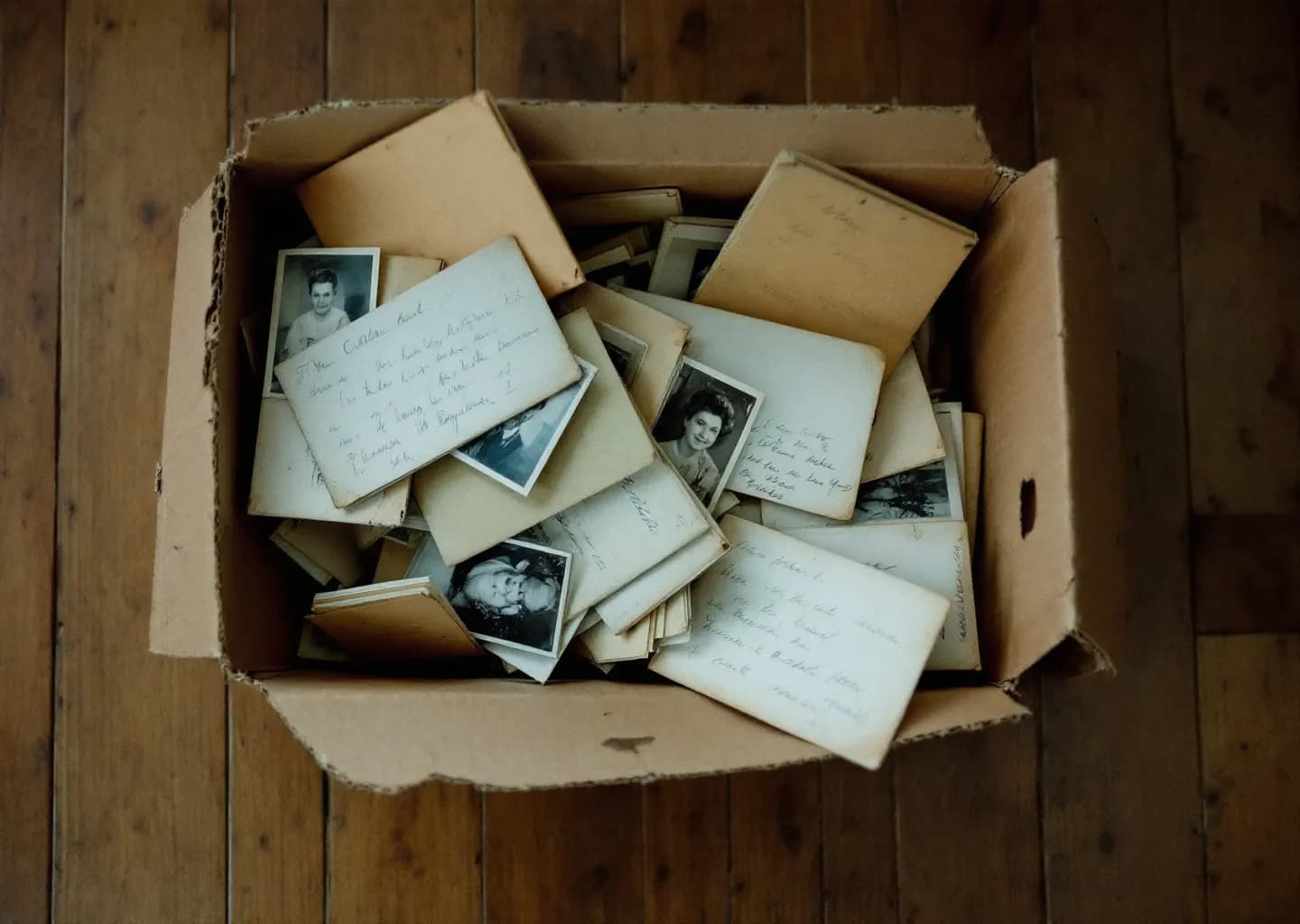Boîte de photographies de famille et d'enveloppes manuscrites renversée sur un parquet