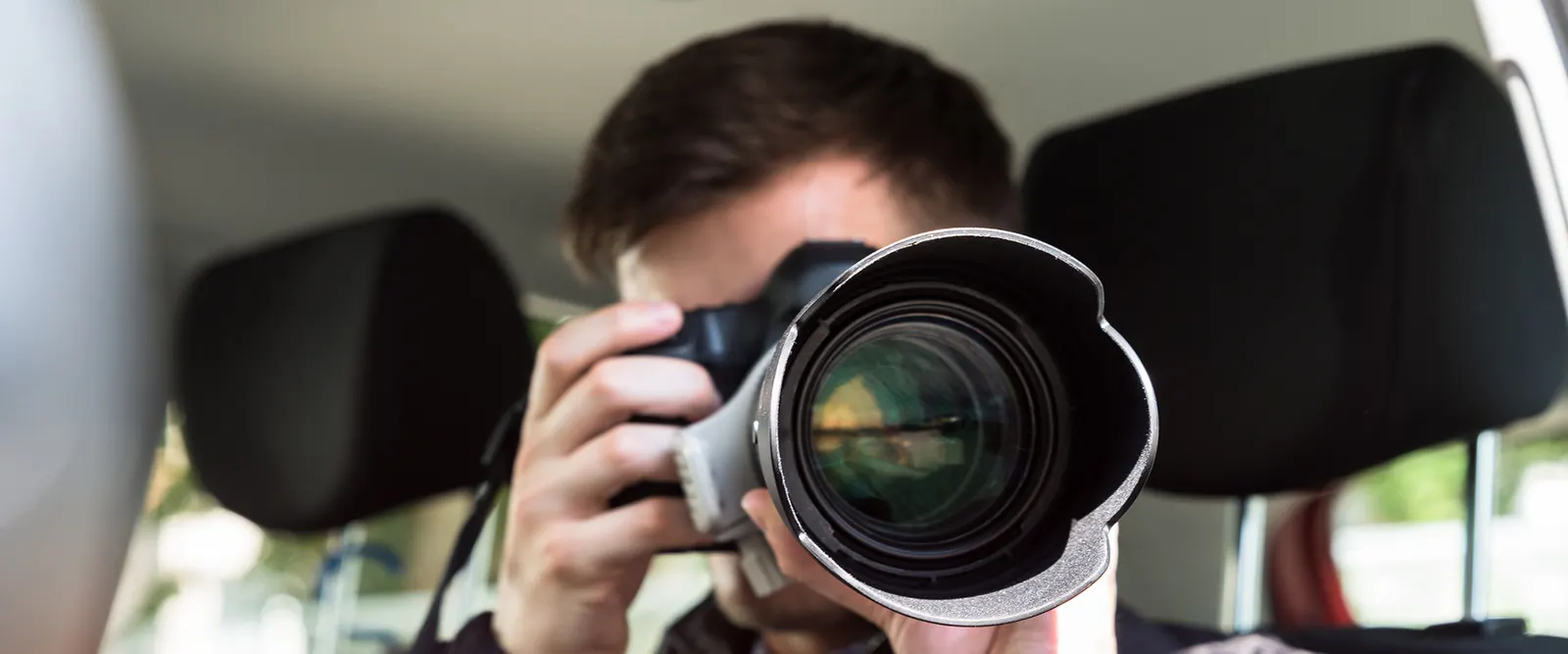 Détective privé photographiant au téléobjectif depuis l'habitacle d'un véhicule