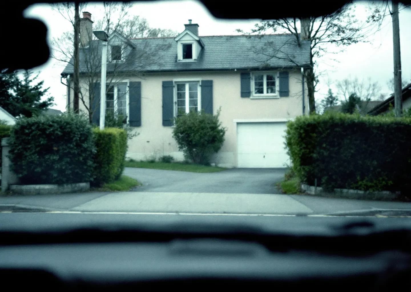 Rue résidentielle vue depuis un véhicule en stationnement, maison aux volets clos en face