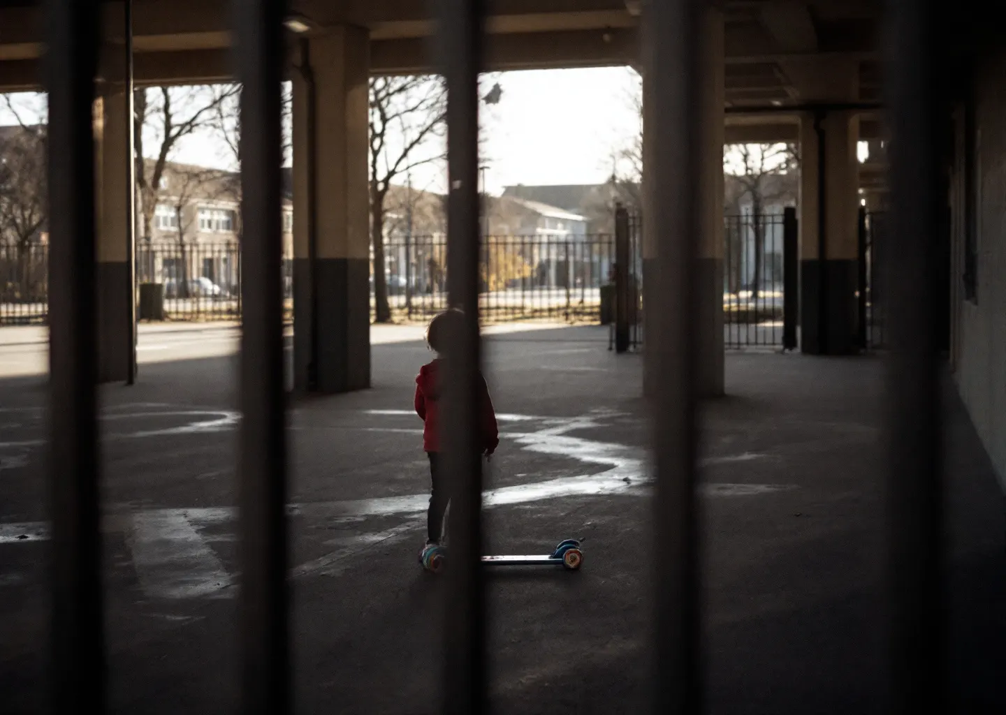Cour d'école déserte en fin de journée vue à travers une grille, trottinette laissée contre un mur