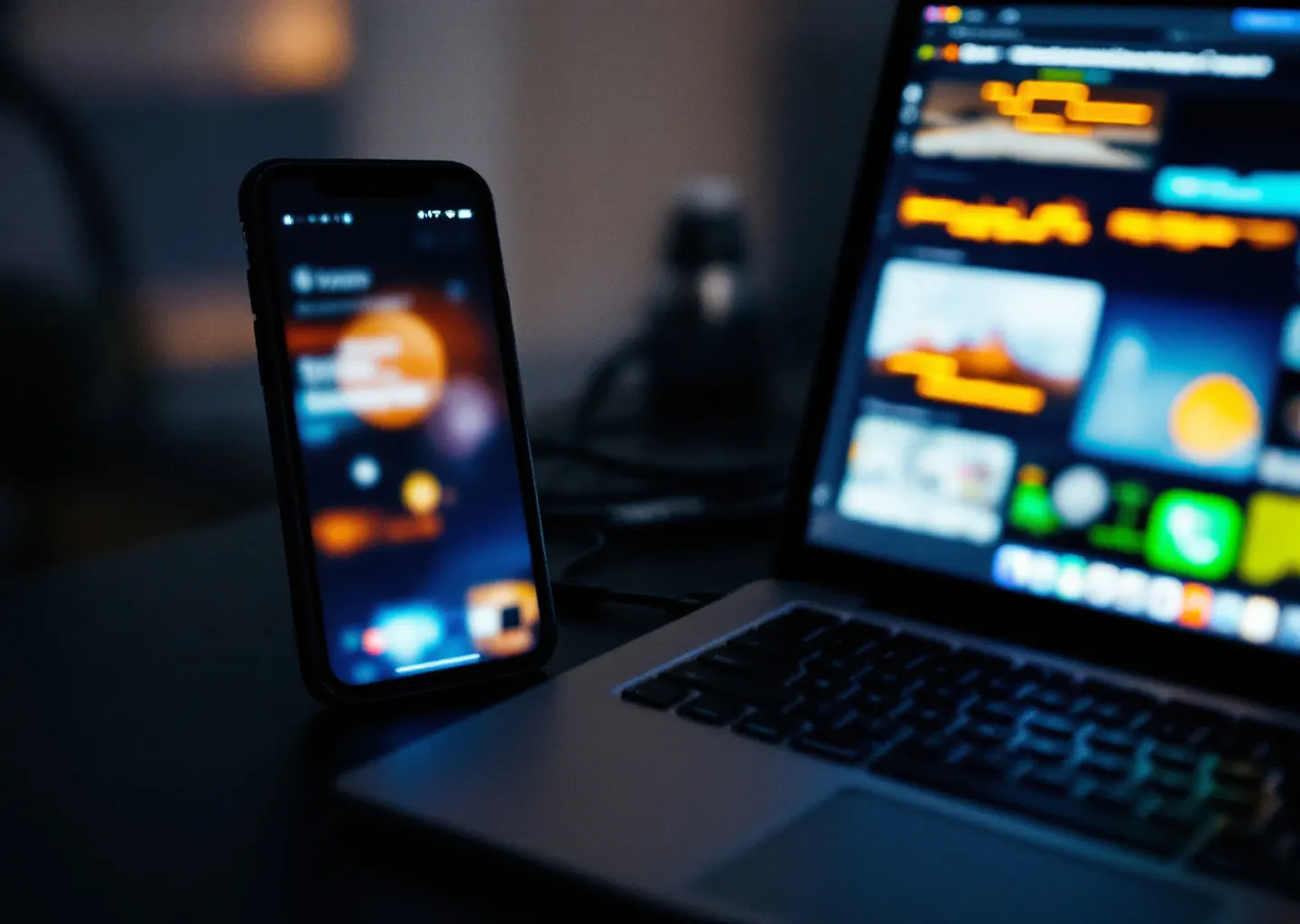 Smartphone et ordinateur portable ouverts côte à côte sur un bureau sombre, reliés par un câble